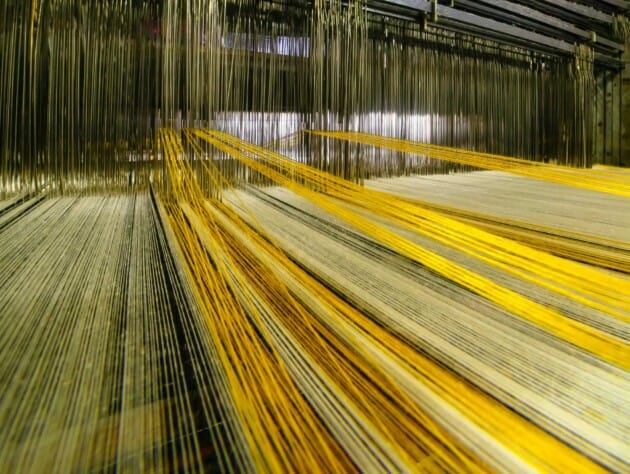 yellow threads being weaved into fabric on industrial loom.